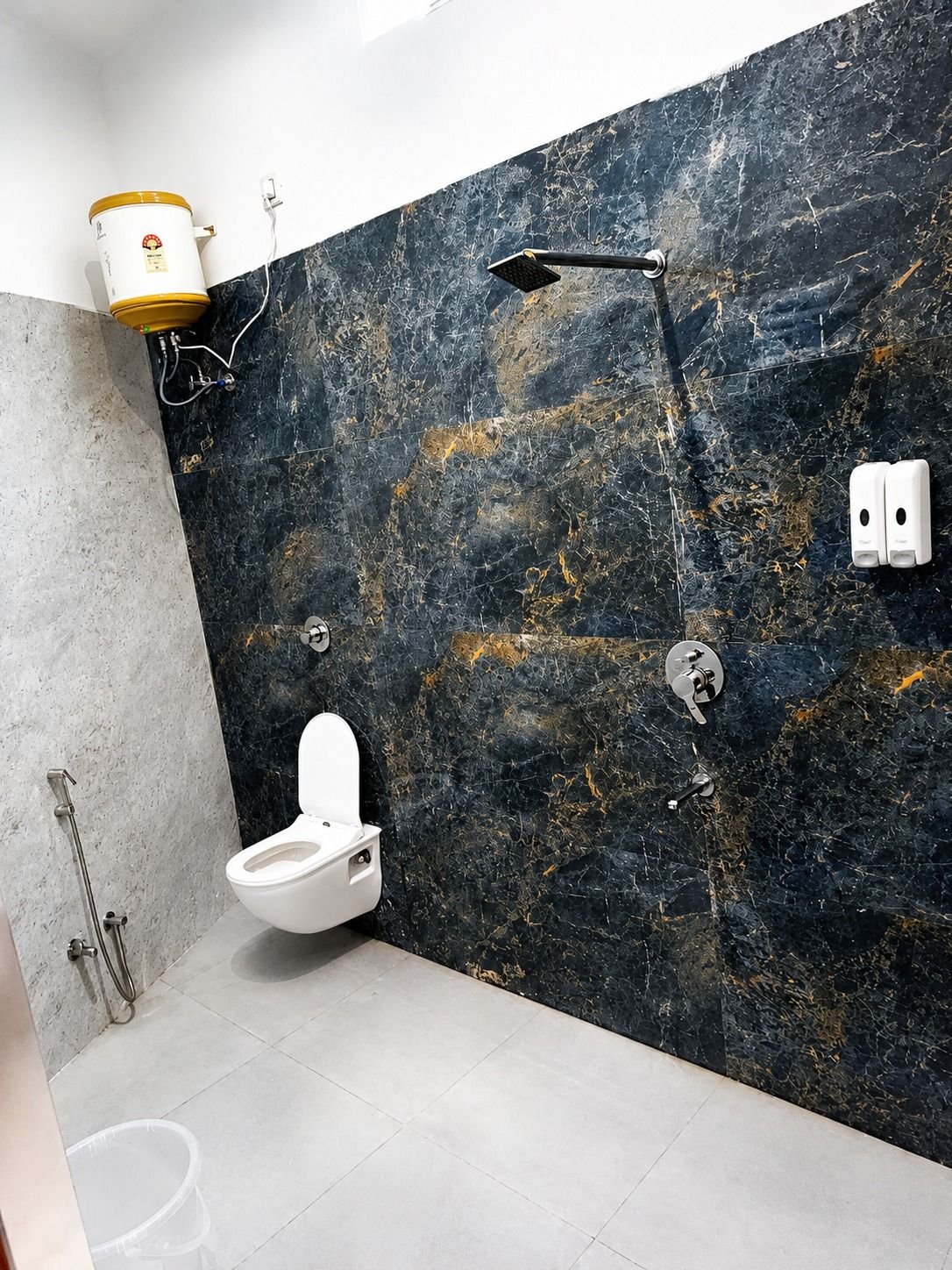 Bathroom with dark marble cladding and geyser at The Ambay Villa Udaipur