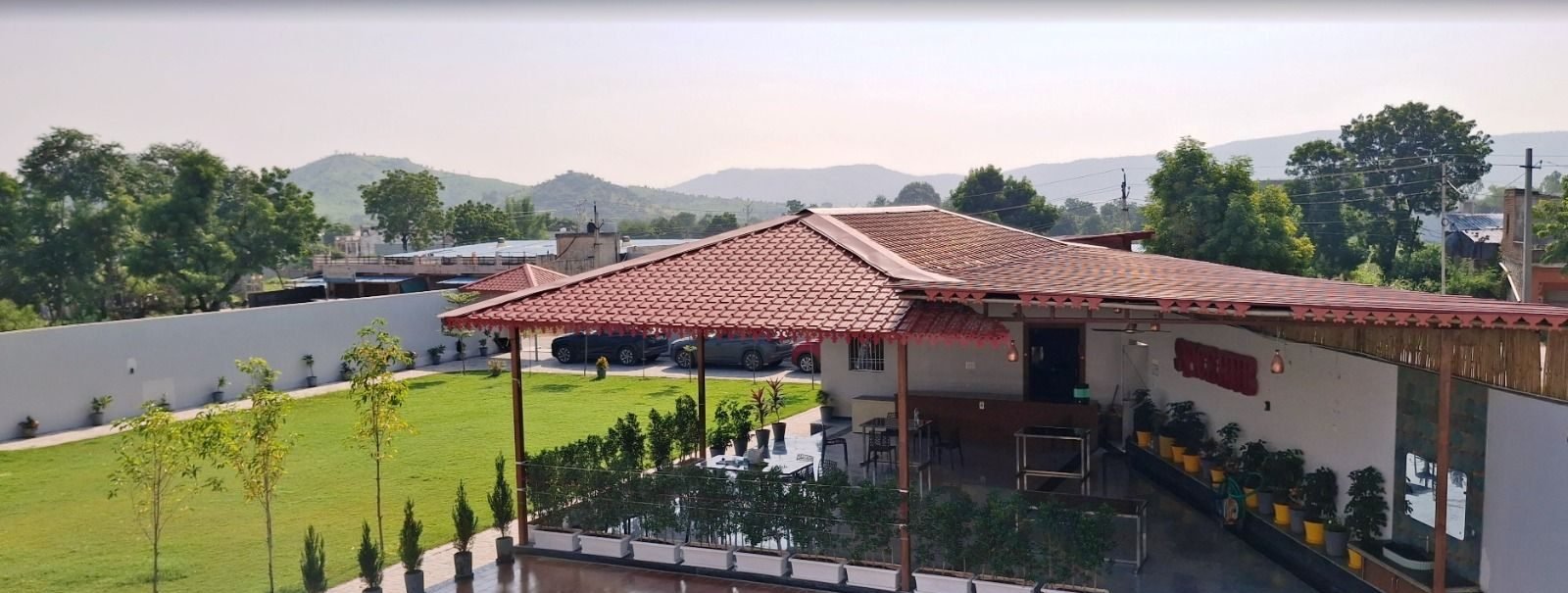 The Ambay Villa resort in Udaipur seen from above — swimming pool, tiled-roof rooms and the Aravalli hills behind
