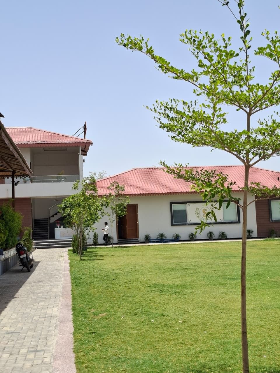 Green lawn at The Ambay Villa Udaipur with the white villa block and terracotta roof behind it